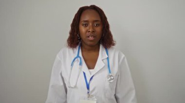 Doktor, genç Afro-Amerikalı kadın sağlık üniforması içinde, pozitif ve mutlu bir gülümseme takınarak, izole edilmiş beyaz arka plan üzerinde onay işareti veriyor.