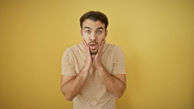 Sarı arka planda sakallı, şaşırmış genç adam izole edilmiş yüz ifadesi sergiliyor..