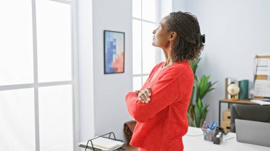 Kırmızılı Afrikalı Amerikalı kadın modern dekor ve bilgisayarla parlak bir ofis düşünüyor..