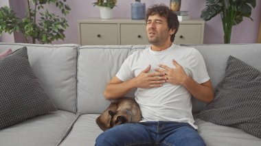 Kanepede rahatsız hisseden genç bir adam, yanında bir siyam kedisi, rahat bir oturma odasında dinleniyor..