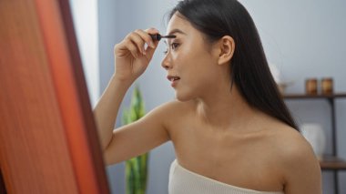 İyi aydınlatılmış bir spa odasında maskara süren bir kadın özen ve güzellik bakımına odaklanıyor.