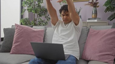 Genç bir İspanyol adam rahat bir oturma odasında dizüstü bilgisayarını kullanmaya ara verirken esniyor..