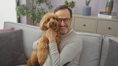 Gülümseyen bir adam rahat bir oturma odasında kanişi kucaklıyor, arkadaşlığı ve ev rahatlığını tasvir ediyor..