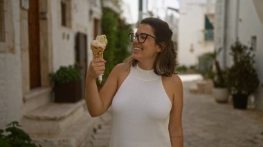 Locorotondo, puglia, Italya, Avrupa 'daki eski şehrin büyüleyici beyaz sokaklarında gezinirken dondurma külahının keyfini çıkaran genç, güzel bir İspanyol kadın..