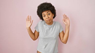 Kafası karışmış kıvırcık saçlı Afro-Amerikan bir kadın pembe bir arka plana karşı duruyor ve belirsizliğini dile getiriyor..