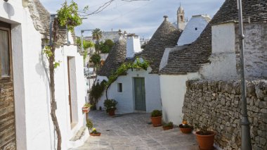 Alberobello 'da büyüleyici bir cadde, güneşli bir günde güneşli bir günde konik çatıları, taş yolları ve canlı saksı bitkileri olan geleneksel beyaz trulli evleri sergiliyor..