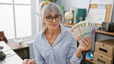 Gri saçlı olgun bir kadın Hong Kong dolarlarını bir ofiste tutuyor ve finansal tema oluşturuyor.
