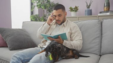 Bir daksund rahat bir oturma odasında kanepede dinlenirken İspanyol bir adam kitap okuyor..
