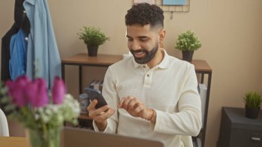 Sakallı, gülümseyen İspanyol adam evde akıllı telefon kullanıyor..