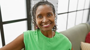 Gülümseyen Afro-Amerikan olgun kadın. Kapalı alanda yeşil giyinmiş.