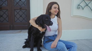 Genç, güzel bir İspanyol kadın şehir sokaklarında siyah labrador köpeğiyle oturuyor. İkisi de şehrin atmosferinin keyfini çıkarıyorlar..