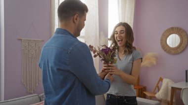 Oturma odasında erkeğin çiçeklerini alan kadın, mutlu bir şekilde gülümsüyor, sıcak bir atmosfer yaratıyor sevgi ve şefkat dolu sıcak bir yuva ortamında.