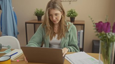 Odaklanmış genç bir kadın rahat bir ofiste dizüstü bilgisayarda çalışıyor bitkilerle ve şık dekorlarla..