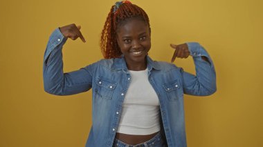 Sarı arka planda kot ceketli, kendine güvenen genç Afrikalı bir kadın neşeli bir gülümsemeyle kendini gösteriyor.