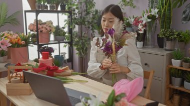 Genç Asyalı bir kadın çiçekçi dükkanında çiçek düzenliyor. Mesleğinin ve yaratıcılığının bir göstergesi olarak..