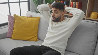 Modern oturma odasındaki koltukta oturan, elleri başının üstünde oturan, şaşkın İspanyol bir adam..