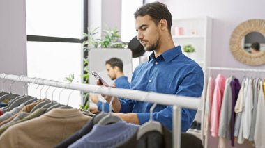 Modern bir elbise odasında ayna ve gardırobu olan akıllı telefon kullanan sakallı genç bir İspanyol..