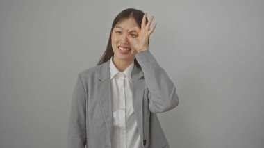 İş kıyafeti giymiş gülümseyen Asyalı bir kadın, beyaz bir arka plana karşı 'tamam' hareketi yapıyor..