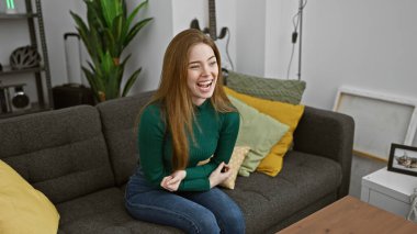 Oturma odasında rahat rahat oturmuş gülen bir kadın, rahat bir stil ve mutluluk yayıyor..