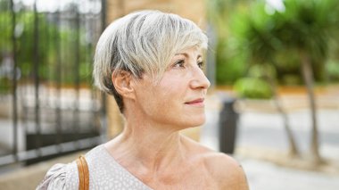 Kısa gri saçlı, olgun bir İspanyol kadın şehir arka planına karşı zarif bir şekilde poz veriyor..