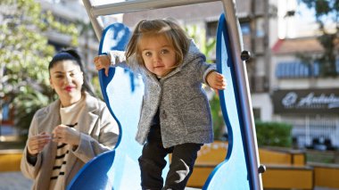 Genç bir kız, annesi onu izlerken parkta kayarak aile eğlencesi ve anne sevgisini yakalıyor..