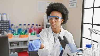 Afrikalı Amerikalı kadın bilim adamı modern bir laboratuvar ortamında bir örnek inceliyor..