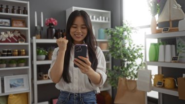 Çin 'de çeşitli dekoratif eşyalarla dolu güzel dekoratif bir dükkânda telefonuna bakarken kutlayan genç bir kadın..