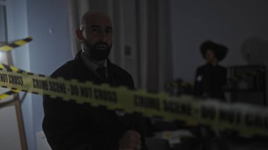 Rozetli bir adam ve bir kadın, ön planda dikkat bandıyla kapalı bir suç mahallinde..