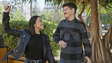 Mutlu bir çift, şehir caddesinde neşeyle dans eder. Palmiye ağaçlarının arka planında sevgi ve arkadaşlık gösterirler..