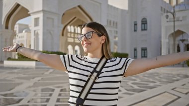 Abu Dabi 'deki Qasr al Watan Sarayı' nın önünde kollarını açmış mutlu genç bir kadın..