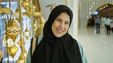 Alışveriş merkezinde süslü lambalarla tesettürlü gülümseyen bir kadın.