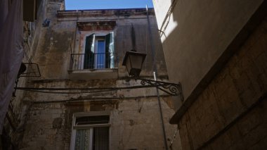 Bari, İtalya 'da güneşli bir günde sokak lambası ve balkonu olan eski taş binalar, Puglia' nın dar sokaklarının ve Akdeniz mimarisinin cazibesini gözler önüne seriyor..