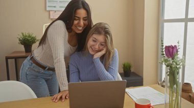 İki mutlu kadın rahat bir ofiste bilgisayarlarını kullanıyor. Bitkilerle ve gün ışığıyla..