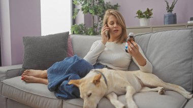 Genç bir kadın evde köpeğiyle koltukta oturuyor, telefonda konuşuyor ve elinde ilaç tutuyor..