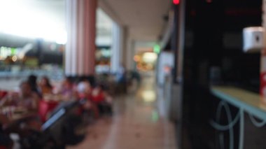 Bokeh geçmişi ve odak dışı koridoru olan bir alışveriş merkezinde oturan bulanık insanlar.