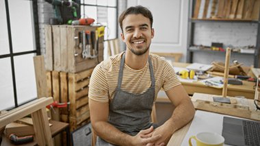 İyi donanımlı bir marangozluk atölyesinde önlük giyen gülümseyen İspanyol bir adamın portresi..