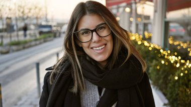 Gün batımında İstanbul 'da bir sokakta duran gözlüklü, gülümseyen esmer kadın, arka planda parıldayan şehir ışıkları..