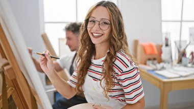 Gülümseyen kadın ve erkek sanatçı, parlak bir sanat stüdyosunda birlikte resim yapıyorlar.