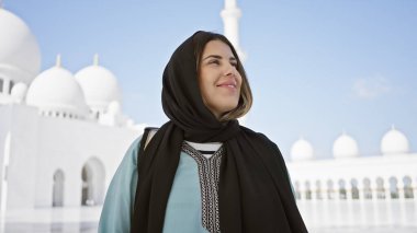 Abu Dabi 'deki Şeyh Zayed Camii' nde tesettürlü gülümseyen bir kadın. Arka planda İslami mimari var..