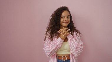 Genç, güzel, kıvırcık saçlı, pembe arka plan duvarından sırıtan, çizgili tişörtlü ve sarı bluzlu bir kadın.