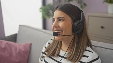 Modern oturma odasında gülümseyen kulaklıklı genç bir kadın.