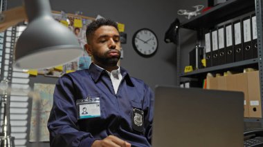 Düşünceli bir Afrikalı Amerikalı erkek dedektif dağınık bir ofiste laptopuyla geç saatlere kadar bir dava üzerinde çalışıyor..