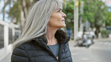 Şehir sokaklarında poz veren gri saçlı, olgun İspanyol bir kadın..