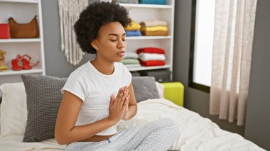 Huzurlu bir Afrikalı Amerikalı kadın yatak odasında meditasyon yapıyor. Evdeki huzuru ve huzuru temsil ediyor..
