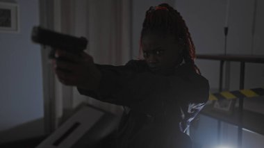 Yoğun, Afro-Amerikan bir kadın loş ışıkta suç mahalline silah doğrultuyor..