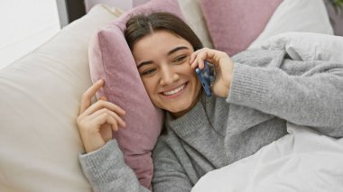 Gülümseyen genç İspanyol kadın evde telefonla konuşuyor.