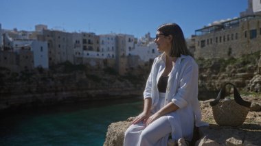 Genç bir İspanyol kadın polignano 'da bir uçurumda dinleniyor. Bir kısrak, puglia, İtalya. Kayalık sahil manzarası ve deniz kenarındaki antik binalar çok güzel..