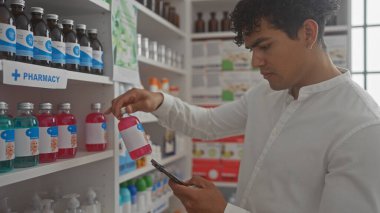 İspanyol bir adam, kapalı bir eczanede akıllı telefonu elinde tutarken ürünü inceliyor..