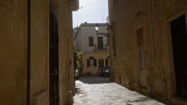Lecce, Puglia, İtalya 'da eski taş binalar, bir sokak lambası, park edilmiş bir bisiklet ve parlak Avrupa güneşinin altında bir araba..