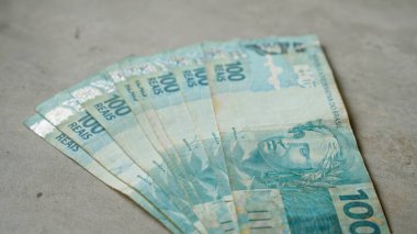 Somut bir yüzeye yayılmış Brezilya 100 reais banknotu ülkenin para ve finans temasını vurguluyor.